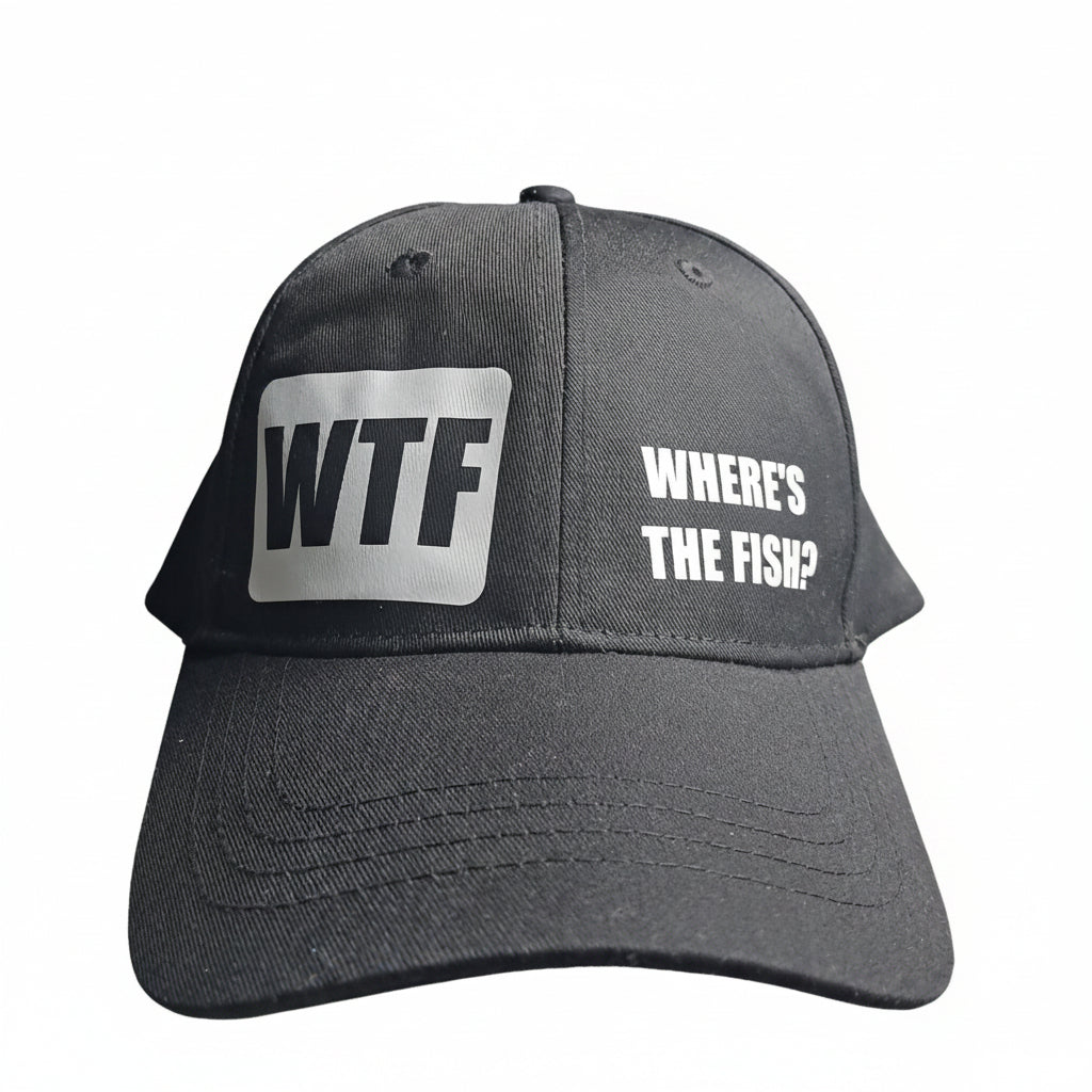 A black baseball cap with a white square patch reading 'WTF' on the front and the phrase 'WHERE'S THE FISH?' printed in white on the side, photographed resting on gray bedding.